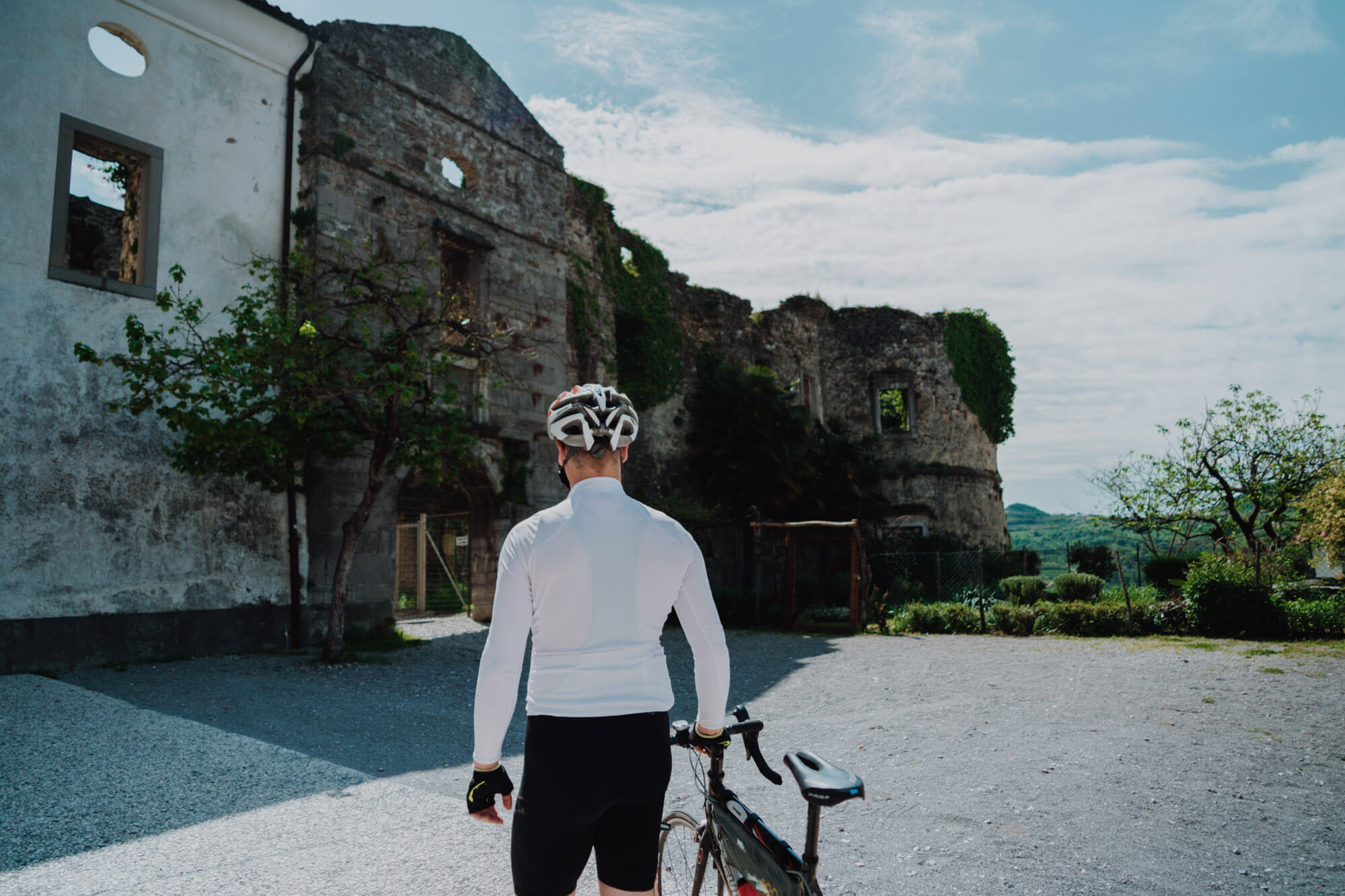 Oseba stoji pred ruševinami, na glavi ima čelado in z roko drži kolo