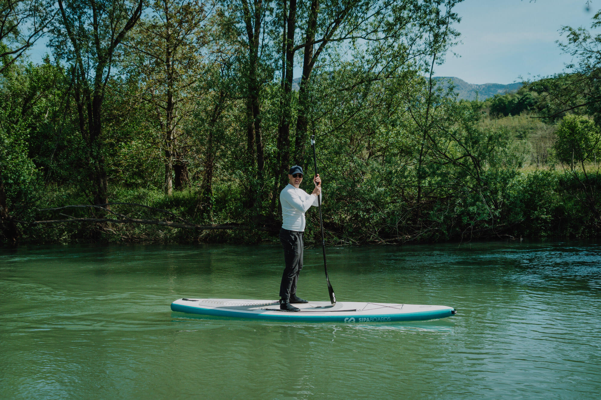 Moški stoji na sup deski, v rokah drži veslo