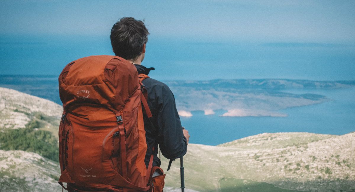 Moški z velikim oranžnim nahrbtnikom gleda razgled na morski zaliv