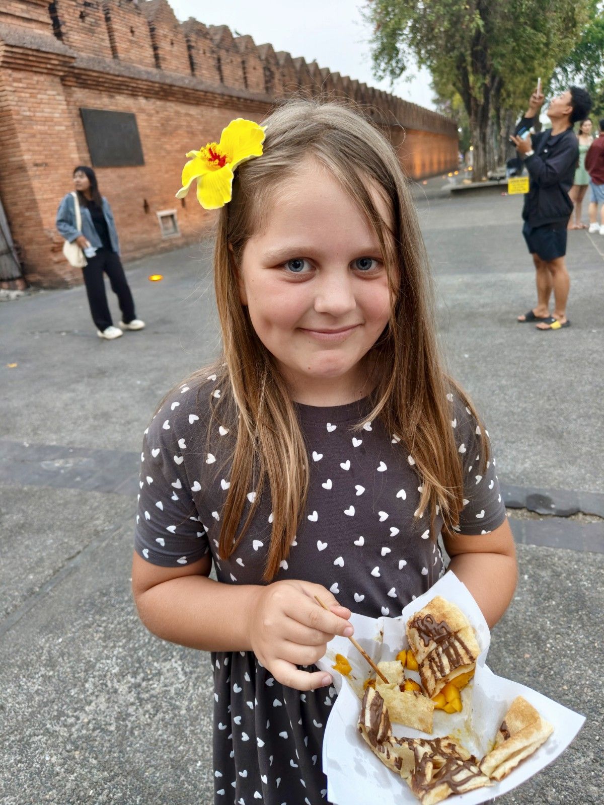 Deklica stoji s azijsko sladico v lončku in se smeji proti kameri.
