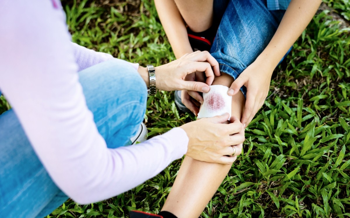 Starš otroku polaga sterilno gazo čez poškodbo na kolenu.