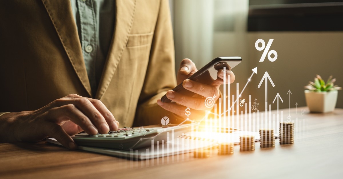 Oseba s telefonom in kalkulatorjem računa prihranke, pred osebo so kovanci in narisan graf za predstavo rasti denarja