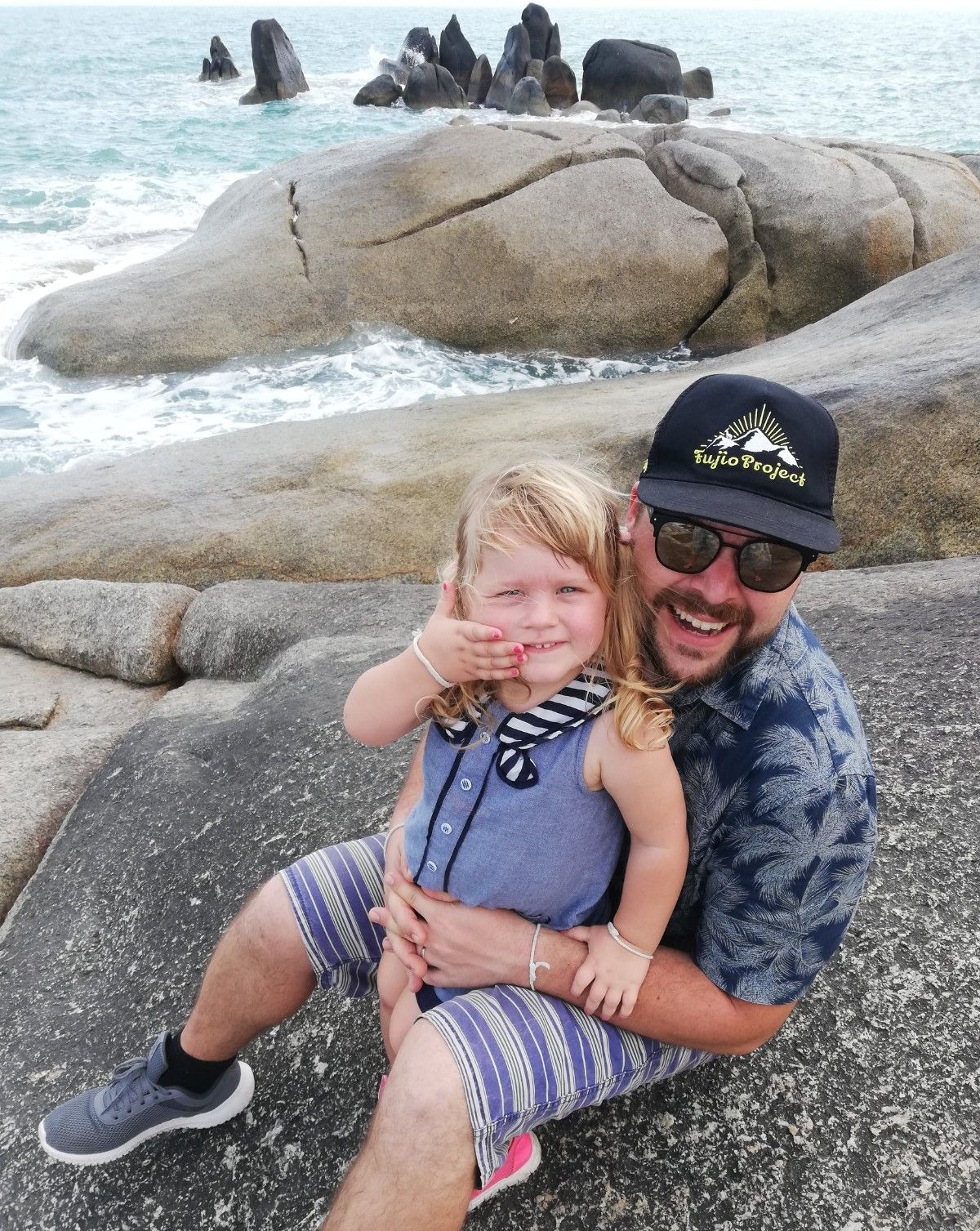 Hčerka in oče sedita na skalah na plaži