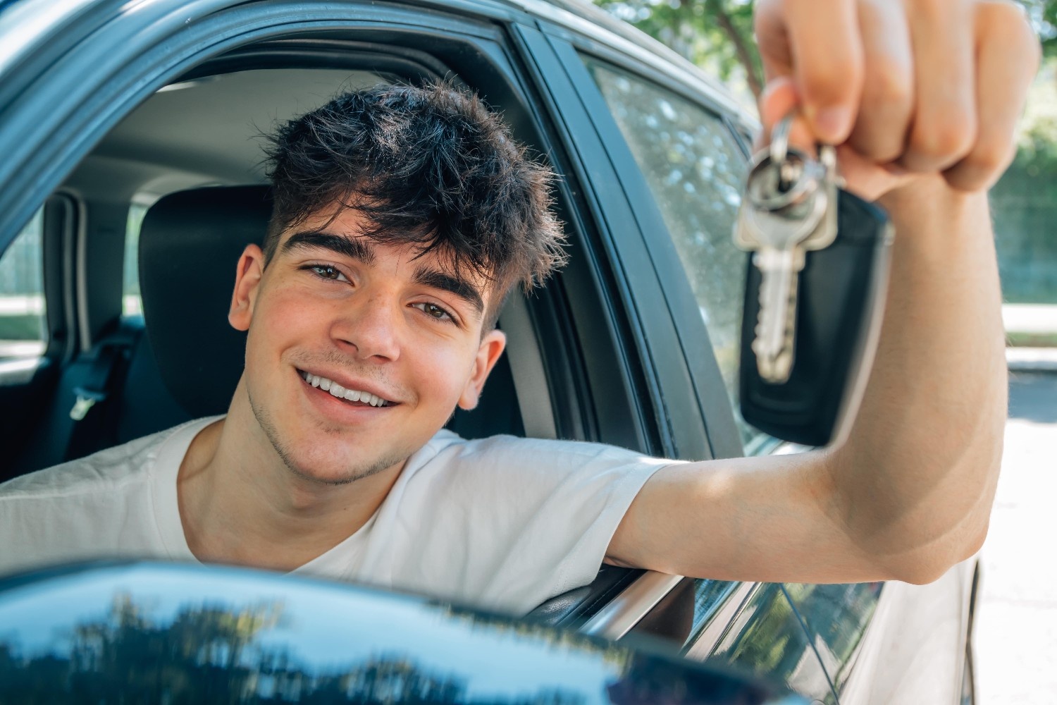 Mladi fant sedi za volanom in veselo drži ključe od avta skozi okno