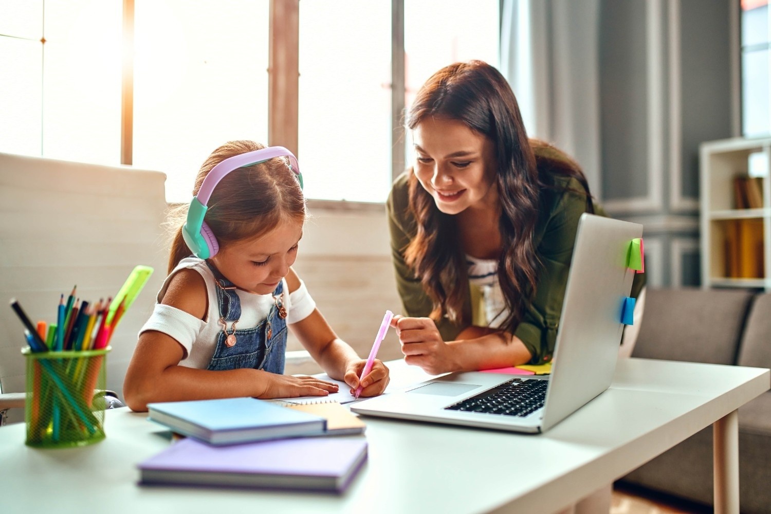 Šolarka s slušalkami rešuje domačo nalogo, pri čemer ji pomaga njena mama.