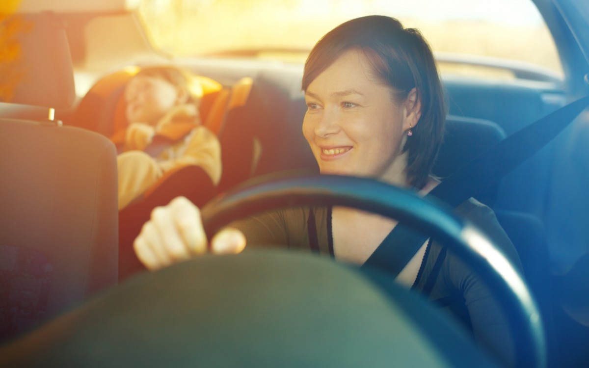 Ženska vozi avto, na zadnjem stolu spi otrok.