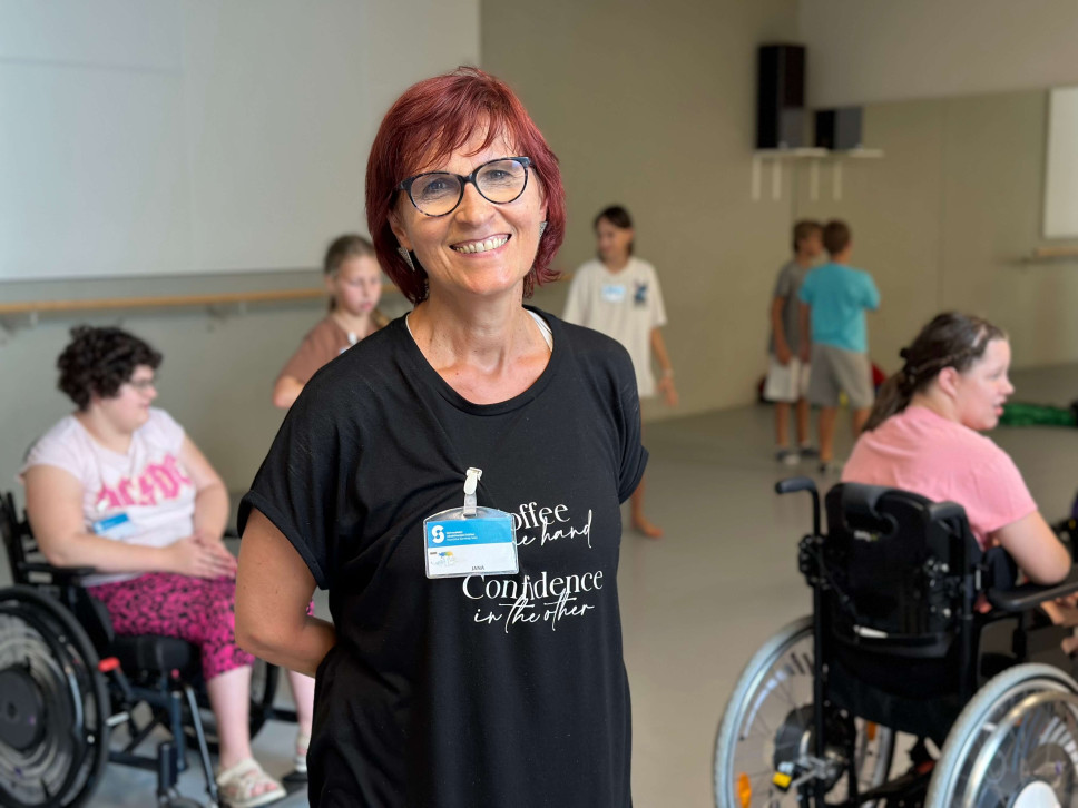 Jana Kovač Valdes stoji sredi plesne dvorane, v ozadju otroci vadijo ples.