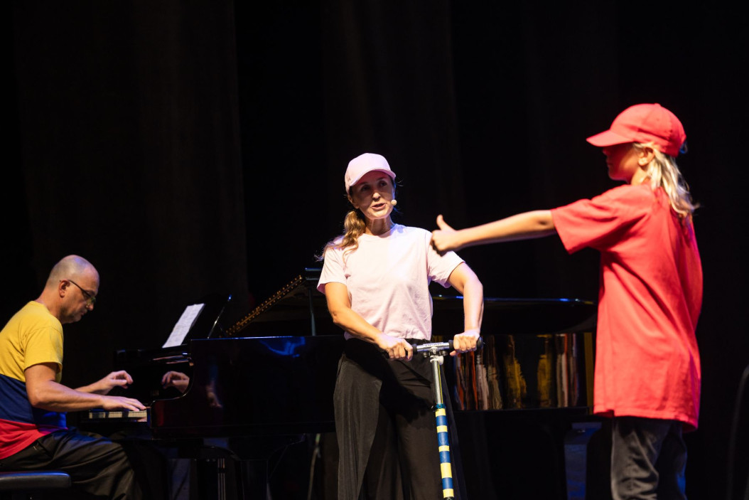 Trije ljudje sredi predstave, eden igra klavir, drugi poje, tretji pleše.