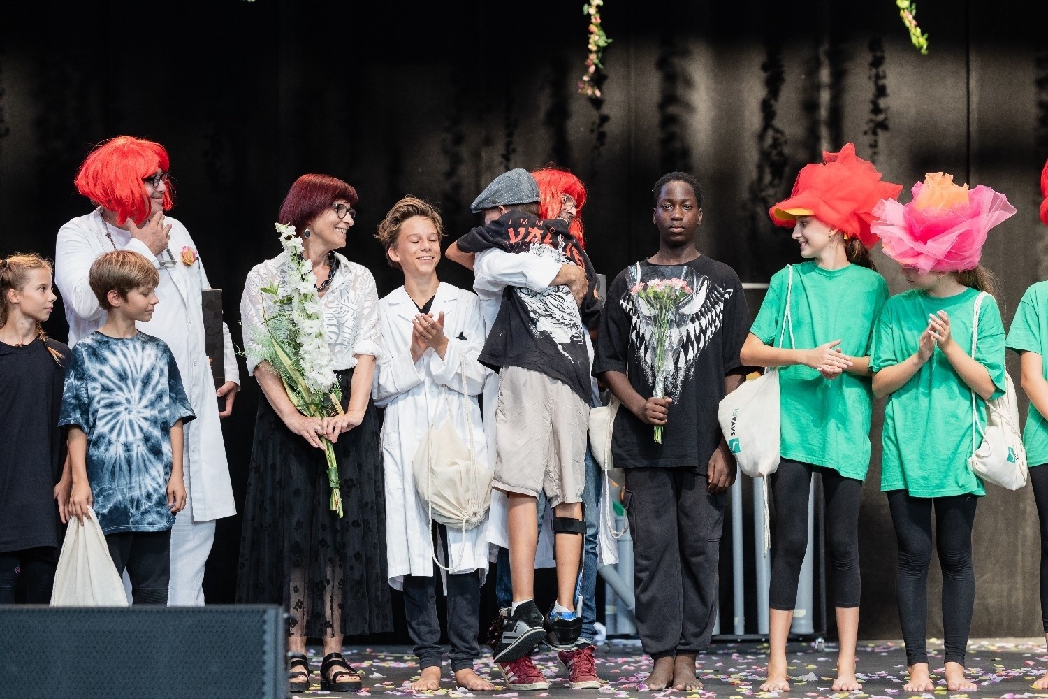 Otroci in odrasli stojijo eden zraven drugega in se poklanjajo aplavzu na koncu plesne predstave.