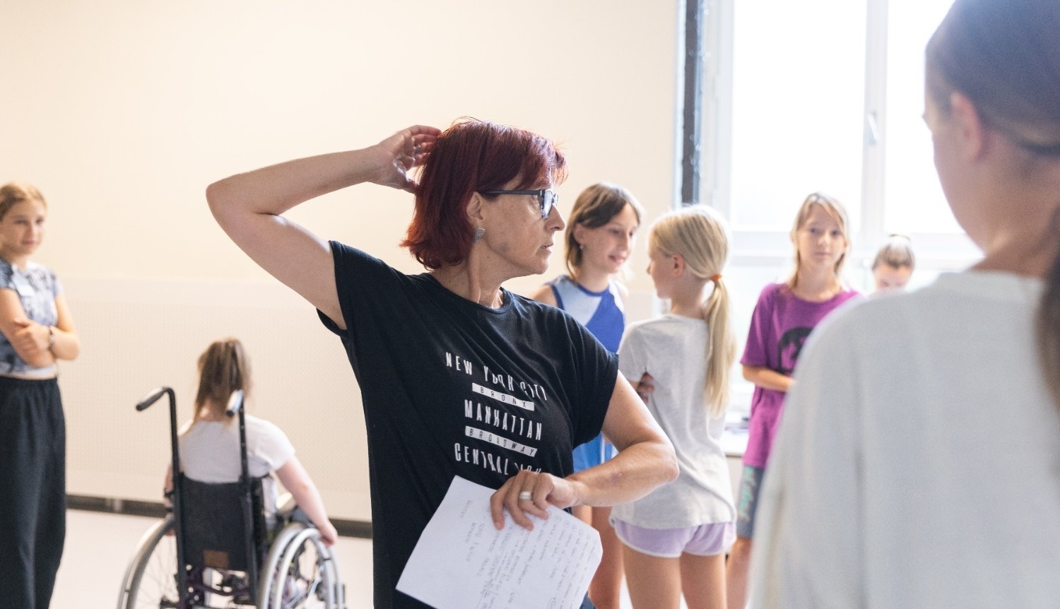 Jana Kovač Valdés stoji v plesni dvorani, v ozadju so otroci