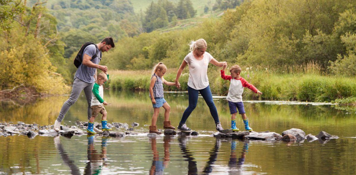 Starša in otroci previdno stopajo po kamnih sredi reke.
