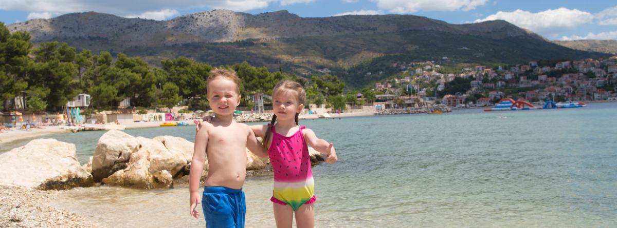 Fantek in punčka v kopalkah stojita na plaži.