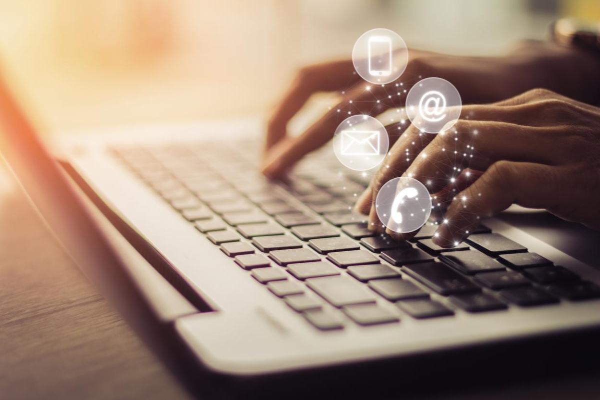 Oseba tipka po tipkovnici prenosnega računalnika, na prstih se pojavljajo različne bele ikone.