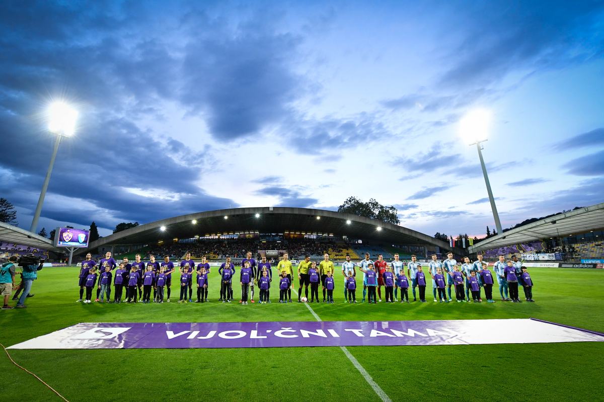 Vsi sodelujoči v nogometni tekmi stojijo na igrišču pred navijači.