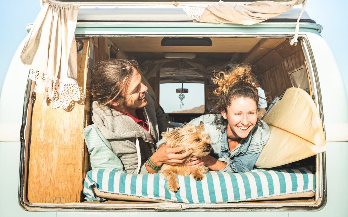 Moški in ženska s psom ležita v avtodomu in se smejita.