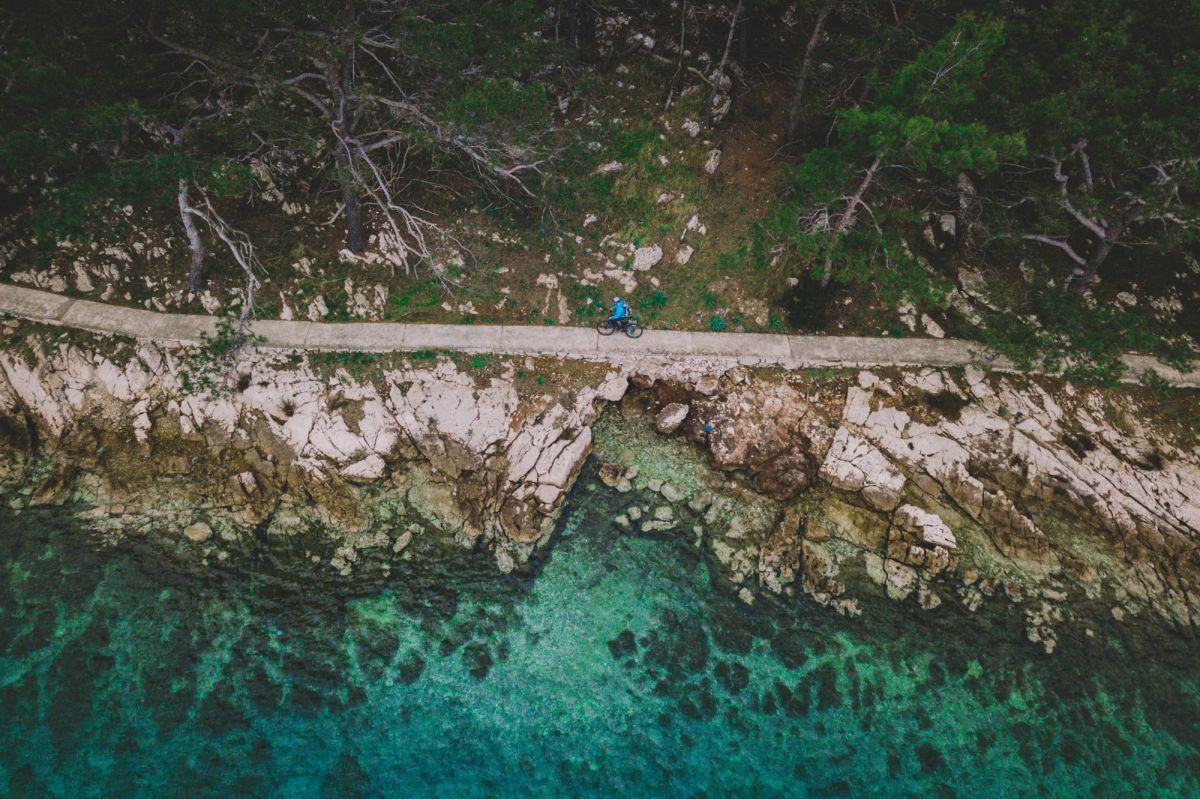 Ptičja perspektiva na kolesarja, ki vozi po poti ob obali.