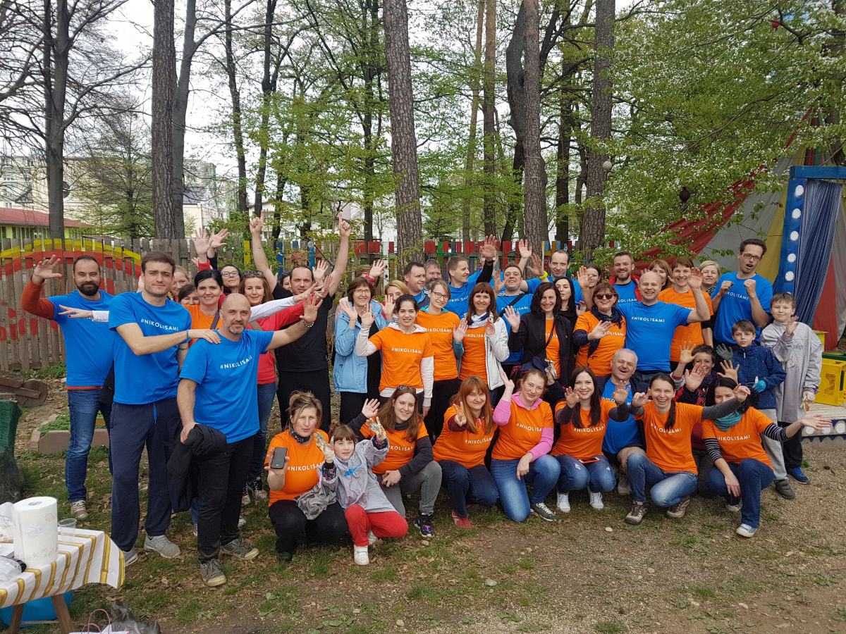 Velika skupina ljudi v oranžnih in modrih majicah pozira za sliko.