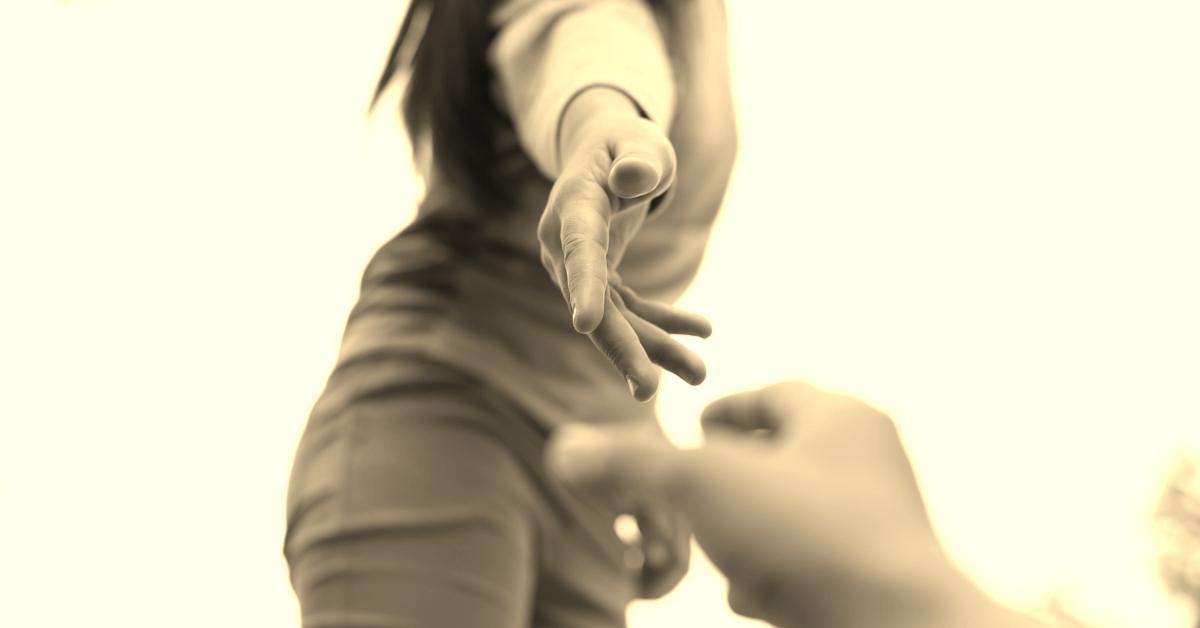 Delno zamegljena slika roke, ki je stegnjena navzdol, da bi pomagala osebi, ki je na tleh.