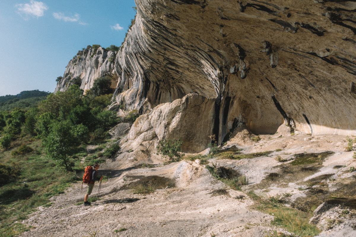 Moški stoji pred zanimivo oblikovanimi skalami sredi narave.