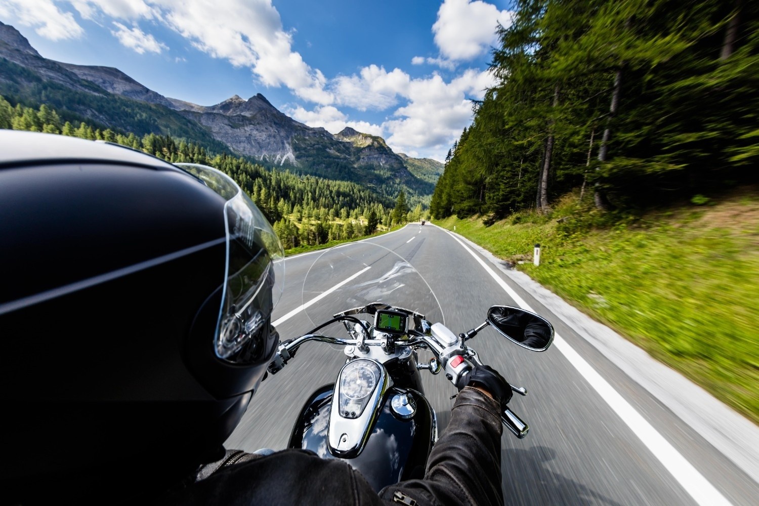 Motorist z motorjem na ravni cesti, okoli ceste je prelepa narava z gozdovi in gorami