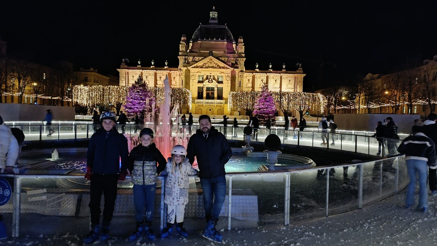 Oče in tri otroci pozirajo pred praznično okrašenim mestom