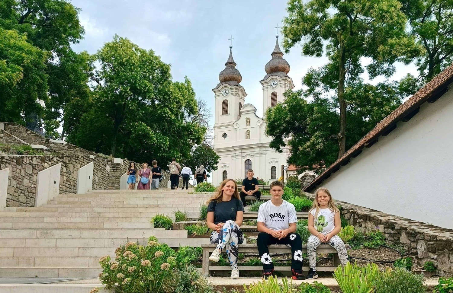 Družina sedi na stopnicah pred belo cerkvijo obkroženo z zelenjem v mestu Tihany na Madžarskem.