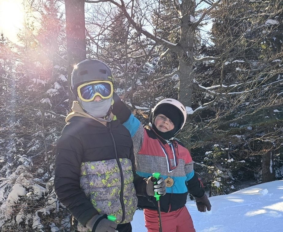 Dva otroka stojita na robu smučišča.