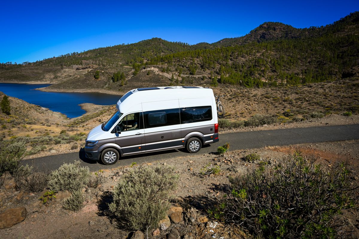 Bel in siv avtodom vozi po cesti sredi narave.
