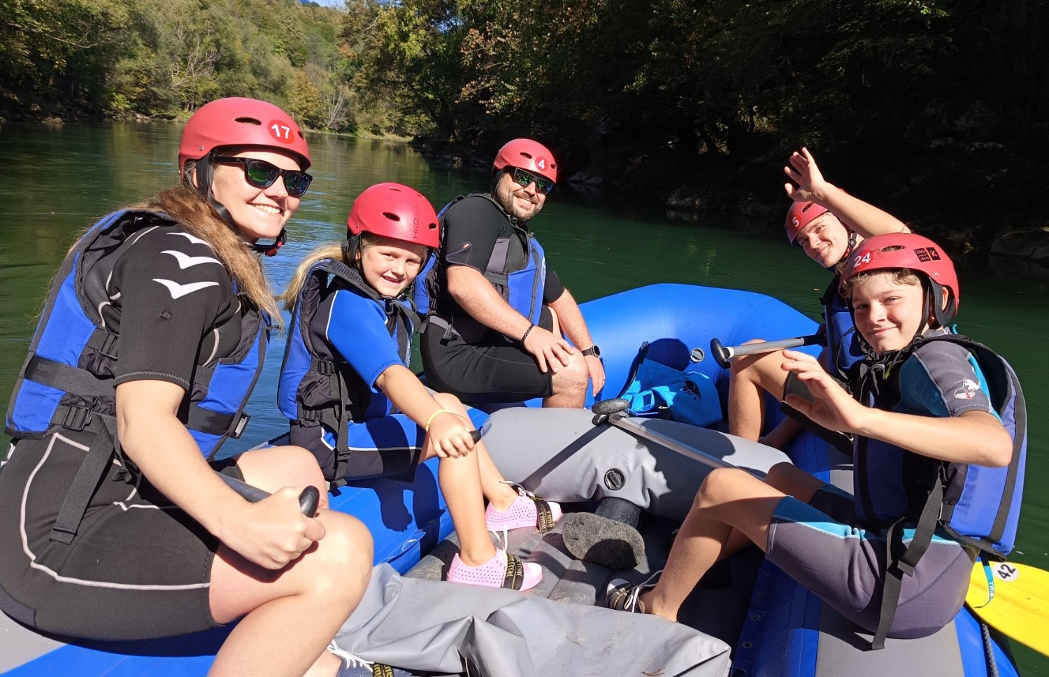 Družina na rafting čolnu na reki, obkroženi z gozdom, pozira za sliko.