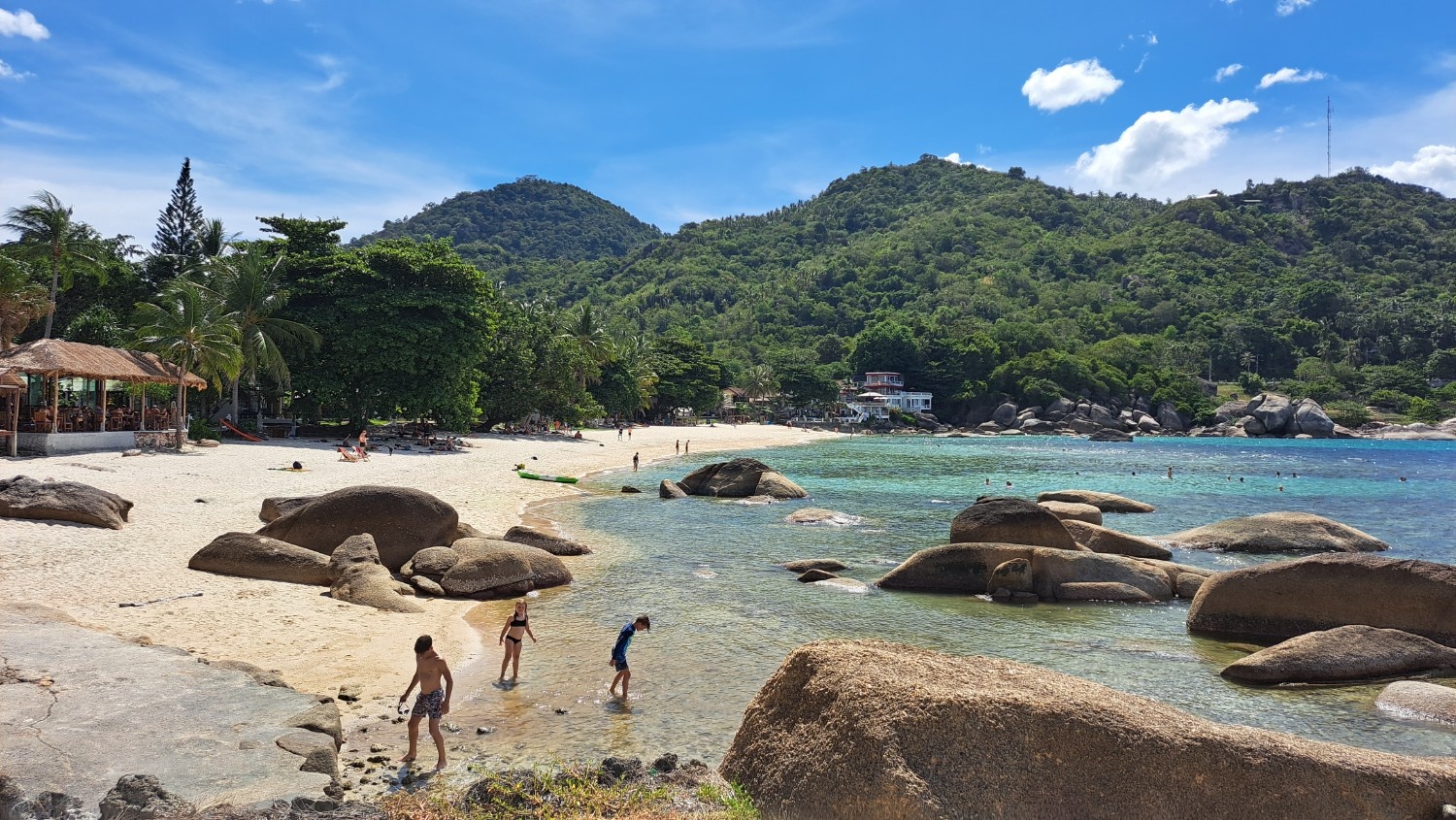 Otroci na tropski plaži, v ozadju so hribi z zelenim gozdom