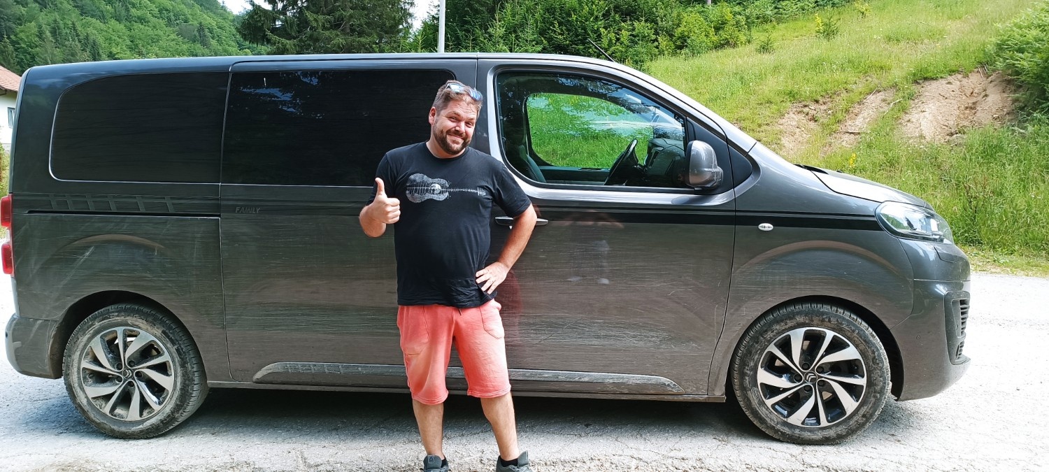 Moški stoji pred avtom in je pripravljen za družinski izlet.