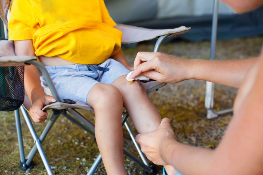 Odrasla oseba čisti rano, ki jo ima otrok na kolenu.