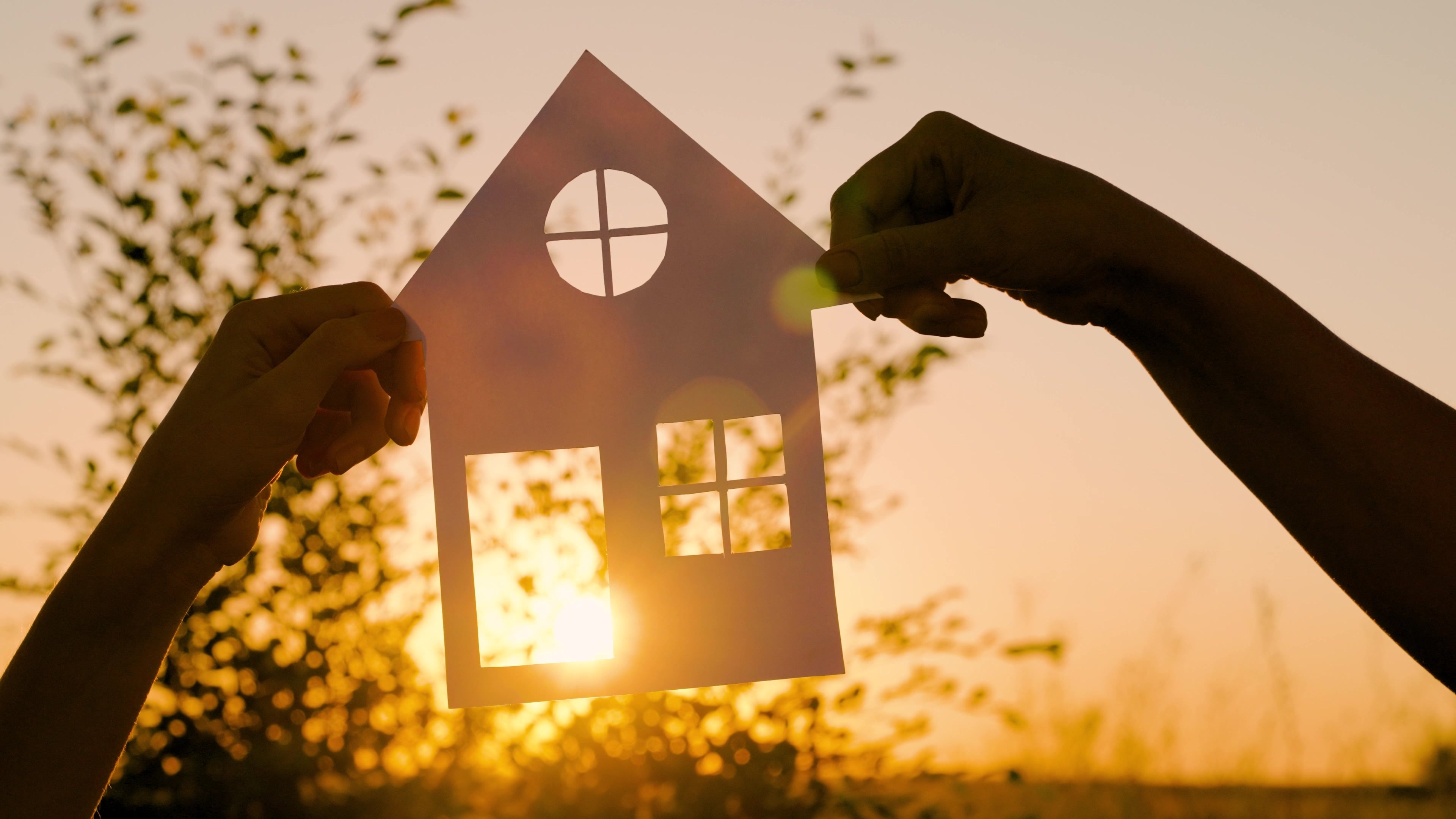 Dve roki držita papirnato hišo pred svetlobo