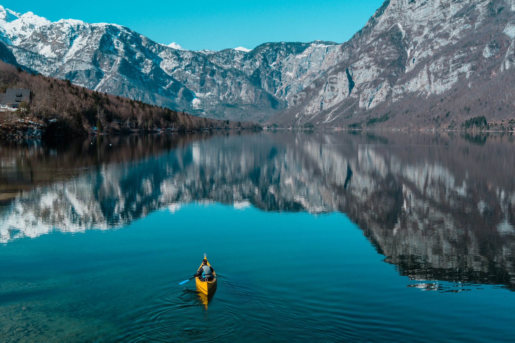 Moški v majhnem kajaku sredi velikega jezera obkroženega z gorami.