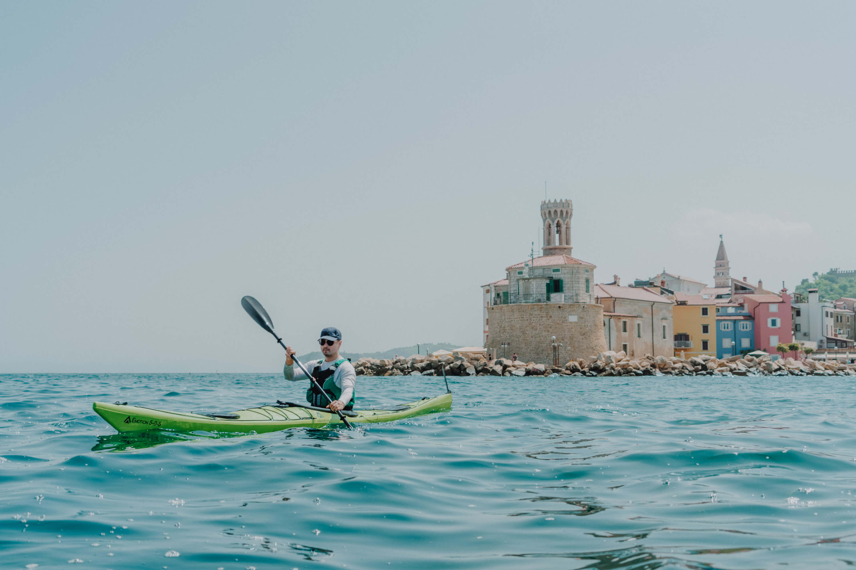 Moški vesla s kajakom stran od obmorskega mesta.