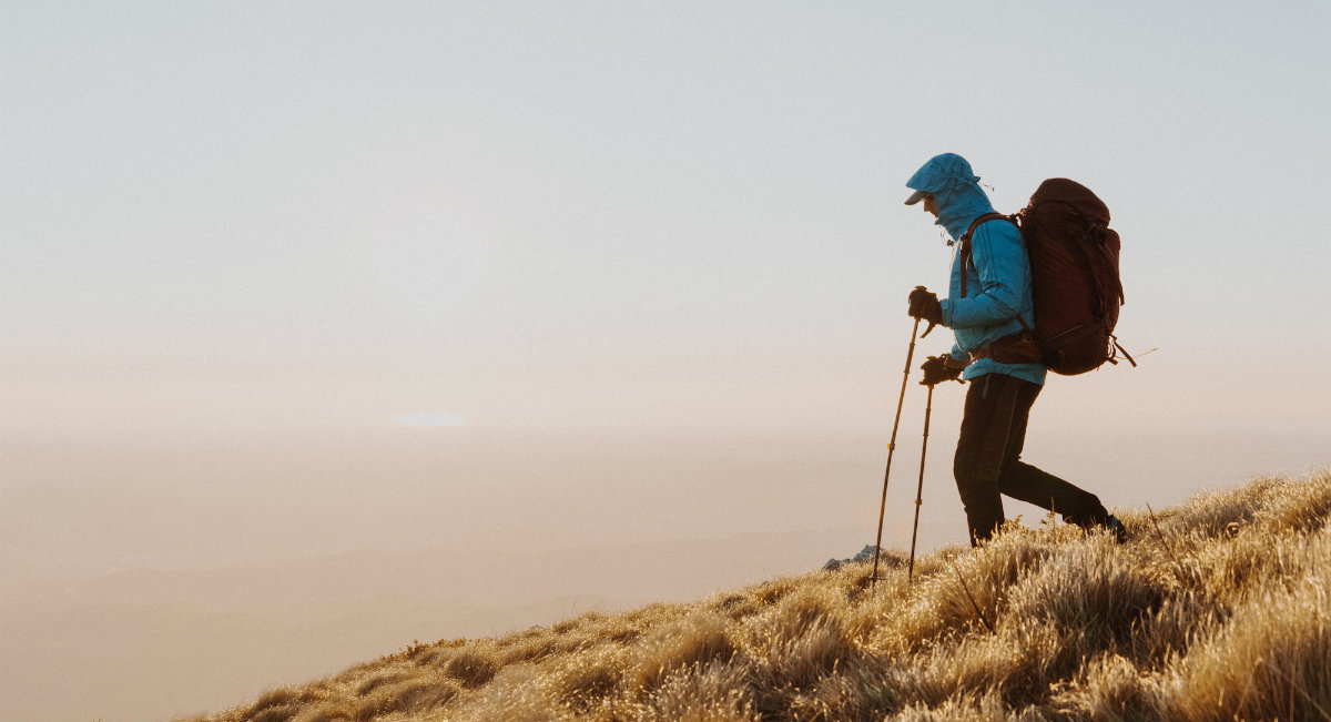 Pohodnik hodi navzdol po hribu, oblečen je v modro vetrovko.