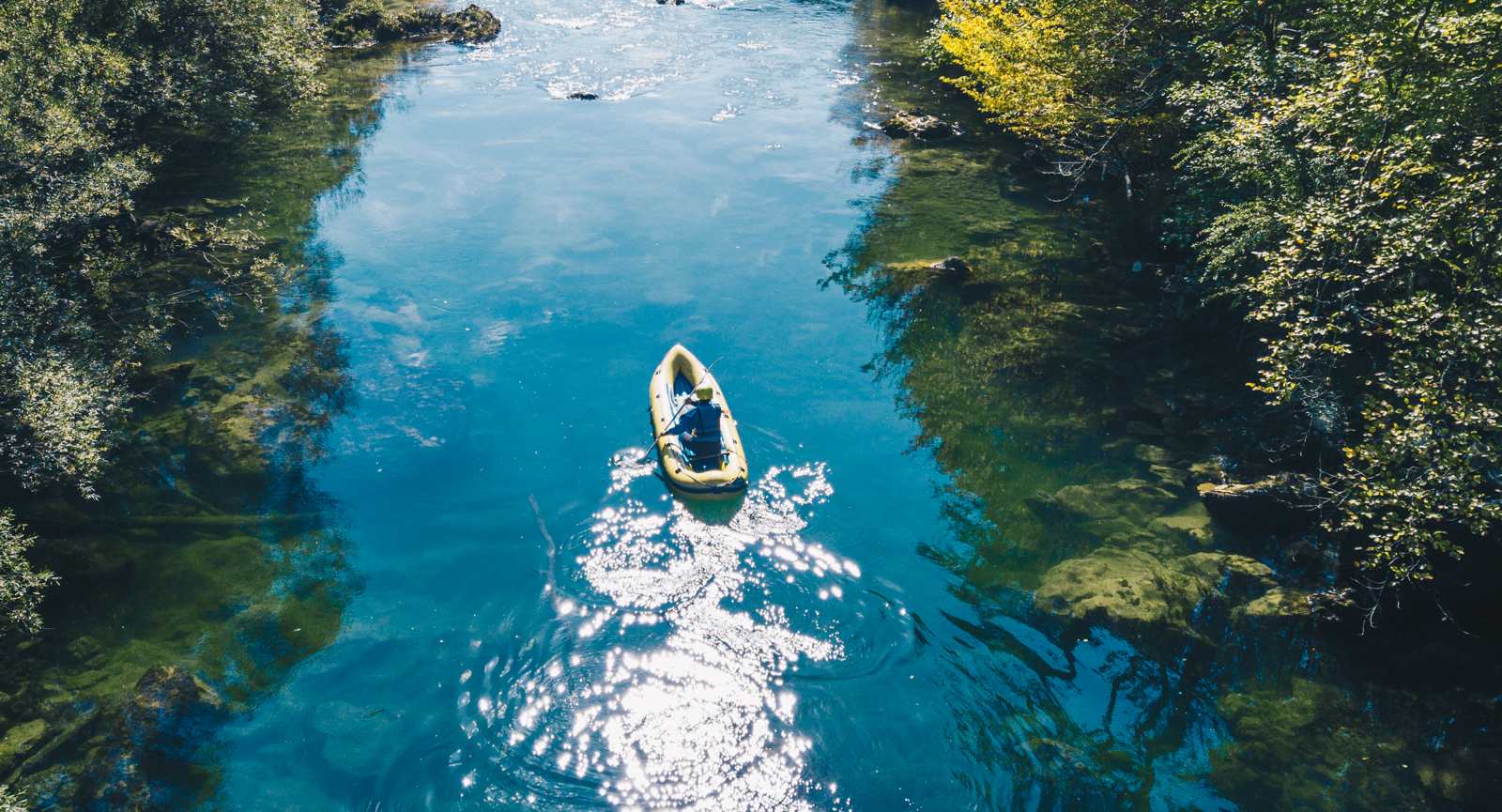 Veslač sredi mirne reke Kolpe, ob straneh so drevesa.