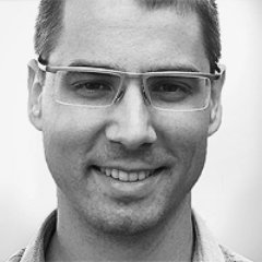 Črno-bela fotografija moškega z očali, ki se smehlja proti kameri